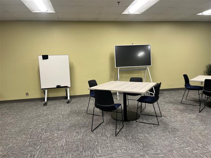 A picture with a table, 4 chairs, a white board and a vibe board